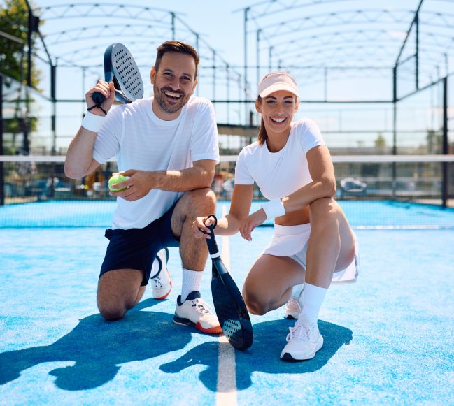 Happy athletic couple playing paddle tennis on outdoor court and looking at camera. Copy space.